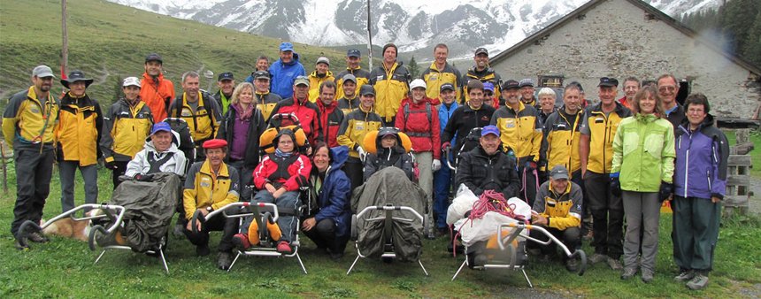 Eine Wandergruppe mit Trecking-Rollstühlen in den Bergen.