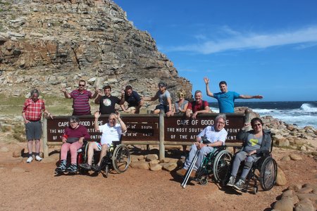 Eine Gruppe von Rollstuhlfahrern mit ihren Begleitpersonen an einer steinigen Küste am Meer